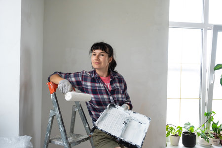 Happy woman in paint roller and white paint for walls in hands close-up portrait. Construction work and cosmetic repairs in house, wall painting, tinting, finishing work with your own handsの写真素材