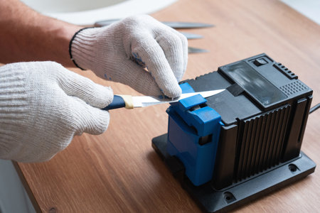 Sharpening a knife on an electric sharpener at home. The man's hand drives the knife blade between the blue sharpeners, dust flies on the machine.の写真素材