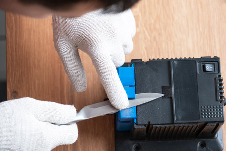 Sharpening a knife on an electric sharpener at home. The man's hand drives the knife blade between the blue sharpeners, dust flies on the machine.の写真素材