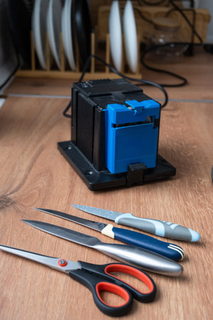 Sharpening a knife on an electric sharpener at home. Flatlay knife blade, scissors, sharpeners, dust...