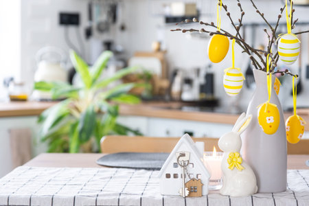 Key to house of cozy home with Easter decor with rabbit and eggs on table of kitchen. Building,...