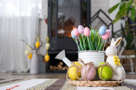 Easter decor near fireplace stove with fire and firewood. Cozy home hearth in interior with potted plans, colorful easter eggs, easter bunny and bouquet. Spring in a country houseの写真素材