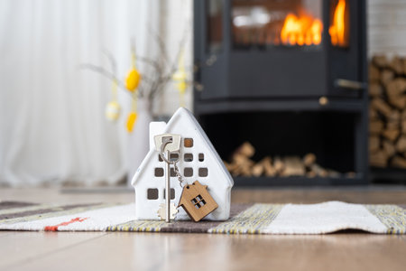 Key to house near fireplace stove with fire and firewood. Cozy home hearth with easter decor, colorful eggs in a basket and bunny. Building, moving, mortgage, rent and purchase real estate, insuranceの写真素材