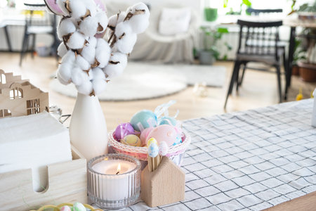 Easter decoration of colorful eggs in a basket and a rabbit on the kitchen table in a rustic style....