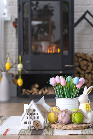 Key to house near fireplace stove with fire and firewood. Cozy home hearth with easter decor, colorful eggs in a basket and bunny. Building, moving, mortgage, rent and purchase real estate, insuranceの写真素材