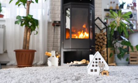 Key to house with keychain against background of fireplace stove with fire and firewood. Cozy home hearth. Building, design, project, moving to new house, mortgage, rent and purchase real estate