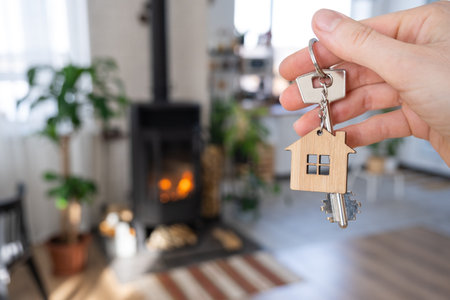 Key to house with keychain against background of fireplace stove with fire and firewood. Cozy home hearth. Building, design, project, moving to new house, mortgage, rent and purchase real estateの写真素材