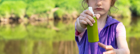 Girl sprays mosquito spray on the skin in nature that bite her hands and feet. Protection from insect bites, repellent safe for children. Outdoor recreation, against allergies. summer timeの写真素材