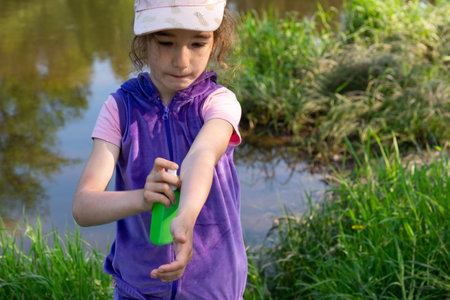 Girl sprays mosquito spray on the skin in nature that bite her hands and feet. Protection from insect bites, repellent safe for children. Outdoor recreation, against allergies. summer timeの写真素材