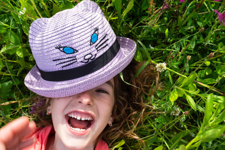 Portrait of a child in a hat with his face covered in summer lying in the grass and wildflowers. Hat with eyes and ears like a cat, summer time, freedomの写真素材