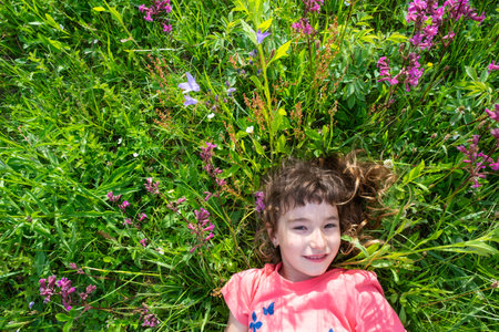 Portrait of a child girl in summer lying in the grass and wildflowers with heels and palms. summer time, freedomの写真素材