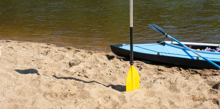 Tourist canoes with paddles stand on the river coast in summer on a water hike. Rafting on inflatable and frame double and triple kayak boats, family trip, extreme adventure in summerの写真素材