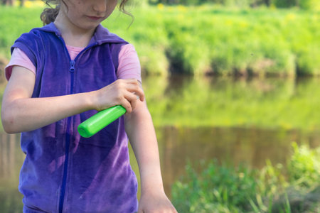 Girl sprays mosquito spray on the skin in nature that bite her hands and feet. Protection from insect bites, repellent safe for children. Outdoor recreation, against allergies. summer timeの写真素材
