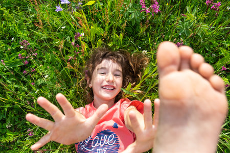 Portrait of a child girl in summer lying in the grass and wildflowers with heels and palms. summer time, freedomの写真素材