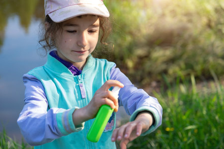 Girl sprays mosquito spray on the skin in nature that bite her hands and feet. Protection from insect bites, repellent safe for children. Outdoor recreation, against allergies. summer timeの写真素材