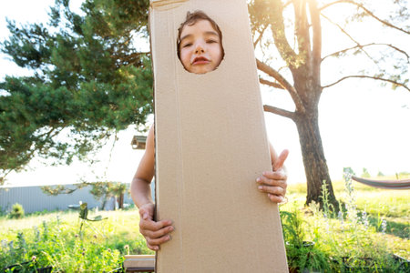 The child is funny dancing and fooling around in a box costume - round cutout for face and hands. Moving to a new house, children's games from improvised means, a suit with your own handsの写真素材