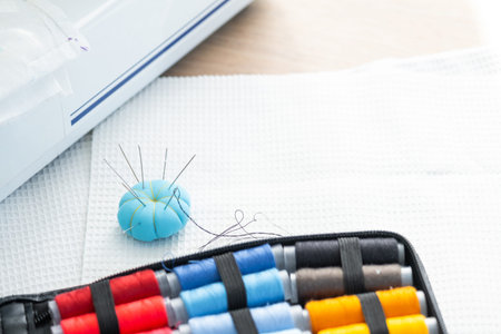 Sewing layout with multicolored spools of thread close-up, needles, electric sewing machine. Filling...