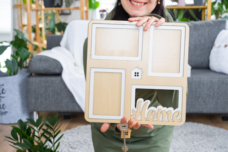 Happy woman in house holds in hands photo frame with figure at home template and key in interior. Dream house project, real estate purchase, insurance, mortgage, rent, reservationの写真素材