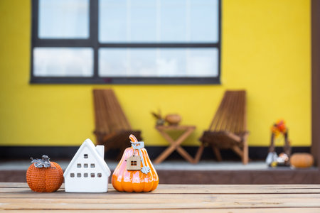 Autumn decor on porch of yellow house outside of pumpkin, lantern, garlands and figure of home and key. Halloween party, autumn mood, Harvest festival, real estate, insurance, mortgageの写真素材