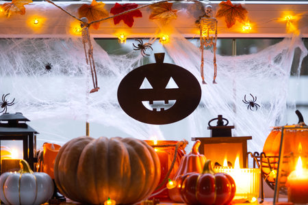 Festive decor of the house on the windowsill for Halloween - pumpkins, Jack o lanterns, skulls, cobwebs, spiders, skeletons, candles and a garland - a cozy and terrible moodの写真素材