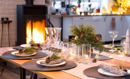 Serving festive table with plates, forks, knives, napkins, glasses close-up near stove fireplace in...
