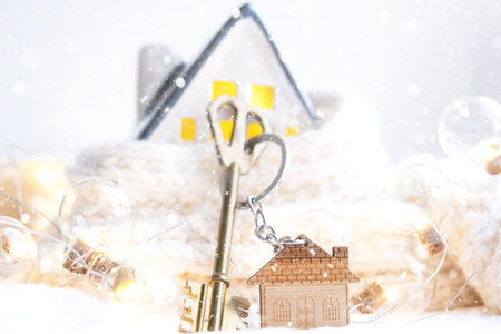 Key to the house with a keychain on a cozy home with a Christmas decor. A gift for New Year, Christmas. Building, design, project, moving to new house, mortgage, rent and purchase real estateの写真素材