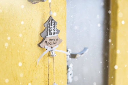 A Christmas tree-shaped pendant with the inscription merry Christmas hangs on the front door of the house on a bell with retro wiring with snow. Copy space