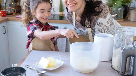 Mom and daughter in the white kitchen are preparing cookies, add ingredients. Family day, preparation for the holiday Christmas, learn to cook delicious pastries, cut shapes out of dough with moldsの写真素材