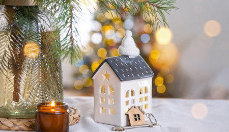 Key and tiny house of a small size on cozy home with Christmas decor on table of festive kitchen. Gift for New Year. Insurance, moving to new house, mortgage, rent and purchase real estateの写真素材