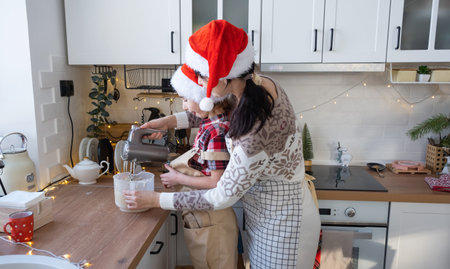 Mom and daughter in the white kitchen knead the dough in the bowl for gingerbread and cookies with a...