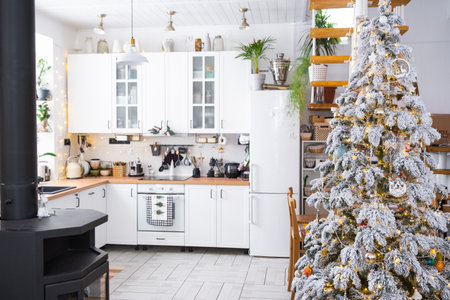 Festive Christmas decor in white kitchen, modern rustic interior with a snowy Christmas tree and fairy lights. New Year, Christmas mood, cozy home. The general planの写真素材