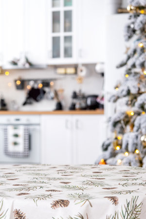 Round empty table to demonstrate the product with tablecloth with pine needles and cones print, space for text in white kitchen, modern interior with a Christmas tree. New Year, Christmasの写真素材