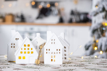 Key and tiny house of a small size on cozy home with Christmas decor on table of festive white kitchen. Gift for New Year. Insurance, moving to new house, mortgage, rent and purchase real estateの写真素材