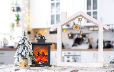Key and tiny house of a small size on cozy home with Christmas decor on table of festive white kitchen. Gift for New Year. Insurance, moving to new house, mortgage, rent and purchase real estateの写真素材
