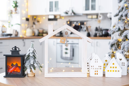 Key and tiny house of a small size on cozy home with Christmas decor on table of festive white kitchen. Gift for New Year. Insurance, moving to new house, mortgage, rent and purchase real estateの写真素材