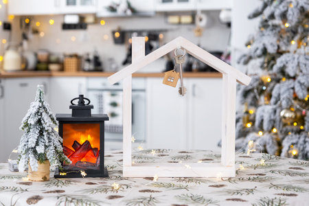 Key and tiny house of a small size on cozy home with Christmas decor on table of festive white kitchen. Gift for New Year. Insurance, moving to new house, mortgage, rent and purchase real estateの写真素材