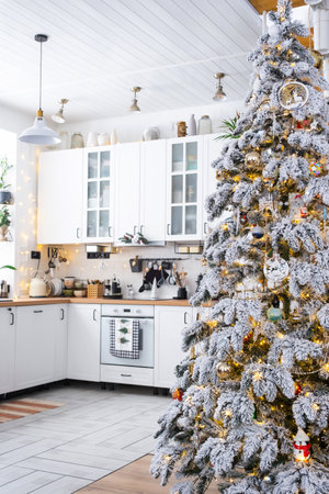 Festive Christmas decor in white kitchen, modern rustic interior with a snowy Christmas tree and fairy lights. New Year, Christmas mood, cozy home. The general planの写真素材