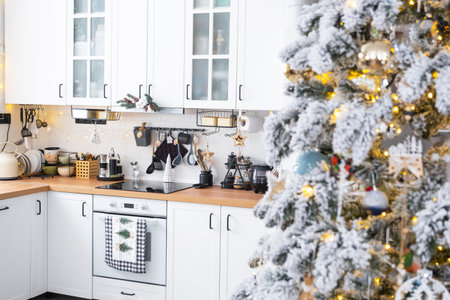 Festive Christmas decor in white kitchen, modern rustic interior with a snowy Christmas tree and fairy lights. New Year, Christmas mood, cozy home. The general planの写真素材
