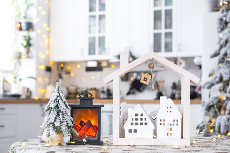 Key and tiny house of a small size on cozy home with Christmas decor on table of festive white kitchen. Gift for New Year. Insurance, moving to new house, mortgage, rent and purchase real estateの写真素材