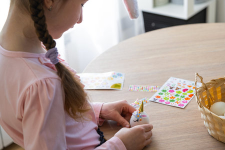 A cute girl with pink bunny ears makes an Easter craft - decorates an egg in the form of a unicorn...