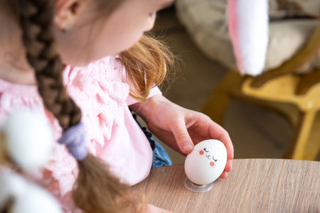 A cute girl with pink bunny ears makes an Easter craft - decorates an egg in the form of a unicorn...