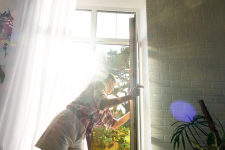 Woman manually washes the window of the house with a rag with spray cleaner and mop inside the...