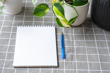 An empty mock up notebook with a pen on a table with home potted plants. Recording recommendations for plant careの写真素材