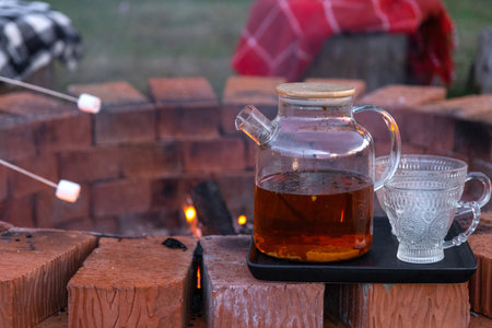 Transparent teapot with tea, cups on a tray on a brick fire pit in the courtyard of the house in a cozy summer evening.の写真素材