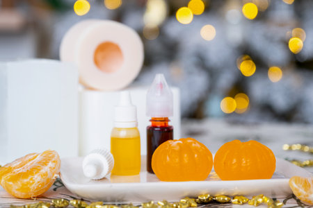 Handmade soap in the form of Orange tangerine with bottles of dye, flavor, a block of glycerin soap base, silicone mold, on background of Christmas tree with golden light. Soap as gift new yearの写真素材