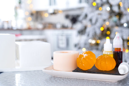 Handmade soap in the form of Orange tangerine with bottles of dye, flavor, a block of glycerin soap base, silicone mold, on background of Christmas tree with golden light. Soap as gift new yearの写真素材