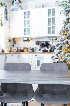 Gray Wooden empty table to demonstrate product with space for text with upholstered chairs in white kitchen, modern interior with Christmas tree and fairy lights. New Year, Christmas mood, cozy home.の写真素材
