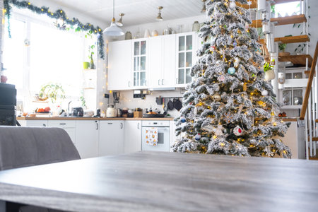Gray Wooden empty table to demonstrate product with space for text with upholstered chairs in white kitchen, modern interior with Christmas tree and fairy lights. New Year, Christmas mood, cozy home.の写真素材
