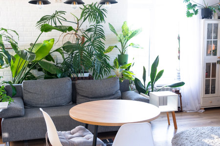 Modern loft-style village interior of house with large potted plants, gray sofa, empty round table, a striped rug, and large windows.の写真素材