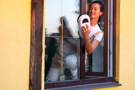 A woman launches window cleaner robot of house outside with a yellow facade. Household robotics,...